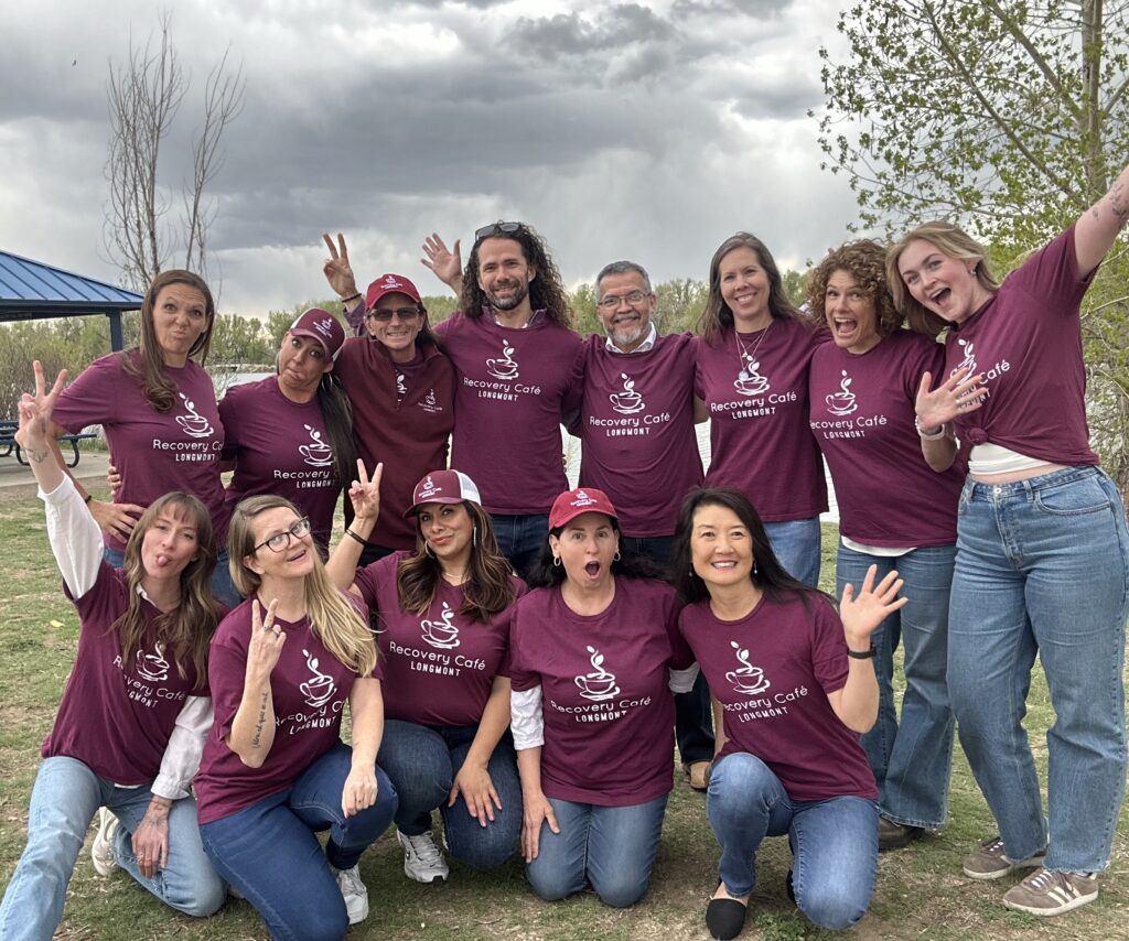 Group of Recovery Café Longmont staff smiling outdoors in matching maroon shirts, representing community, connection, and recovery. Join our team !