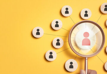 A magnifying glass overlooks many icons of people, representing a job search. It features a yellow background to exude excitement and energy towards the search for a new Executive Director.