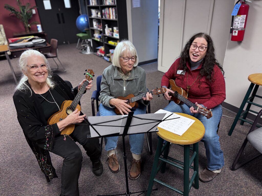 Three women enjoy playing ukulele and singing, building recovery capital through creativity.